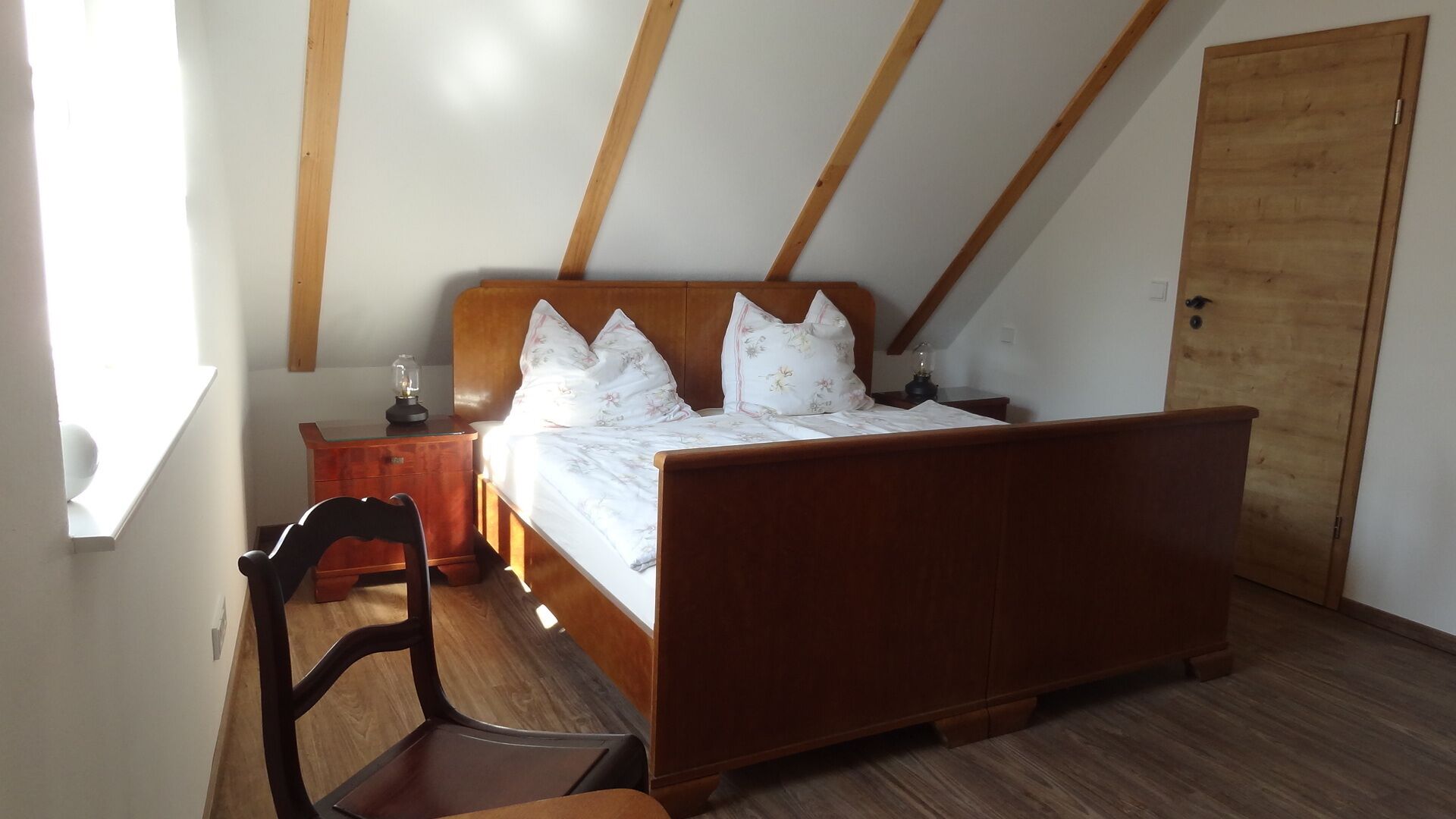 A bedroom with a wooden bed, a nightstand, a chair, and a wooden door.