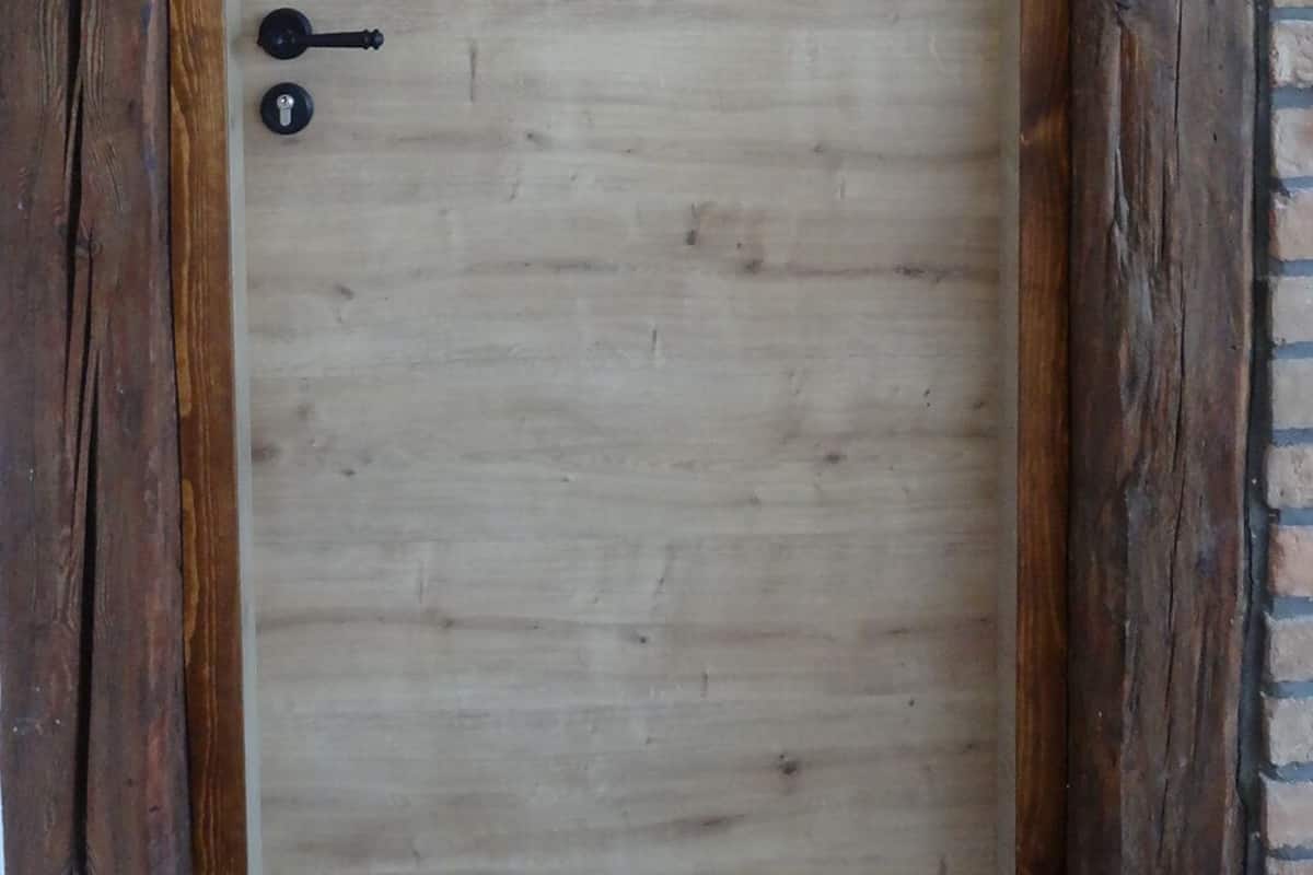 Una puerta de madera con un cerrojo sencillo y una cerradura, enmarcada por vigas de madera rústicas y una pared de ladrillo.