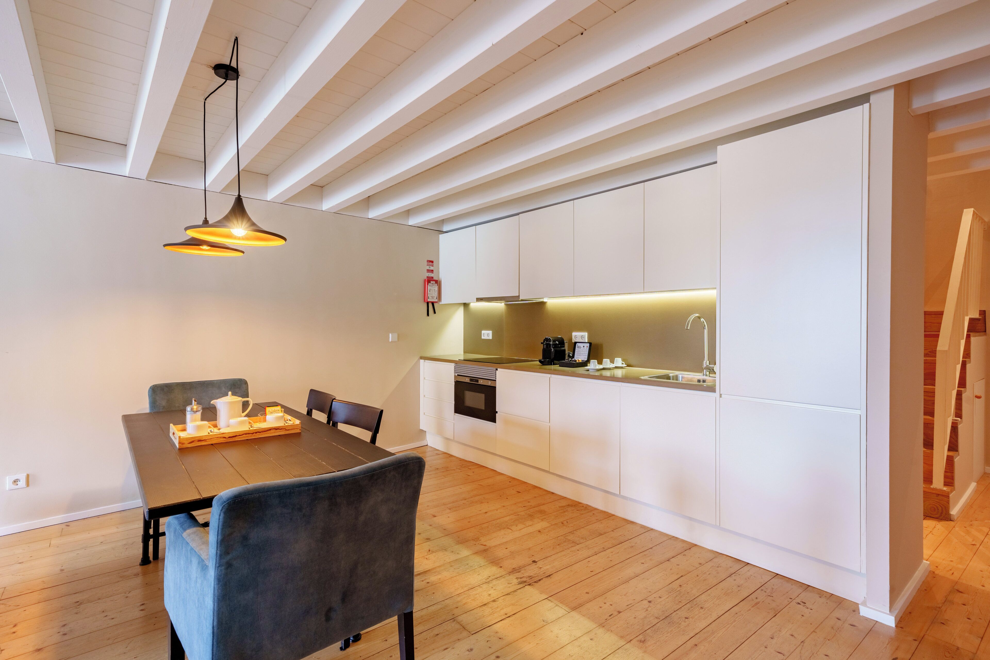 A modern kitchen with white cabinets, a wooden dining table, and a pendant light.