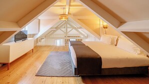 An attic bedroom with a bed, a TV on a dresser, and a view of the house's interior. - Porto Vitoria Apartments (Porto)
