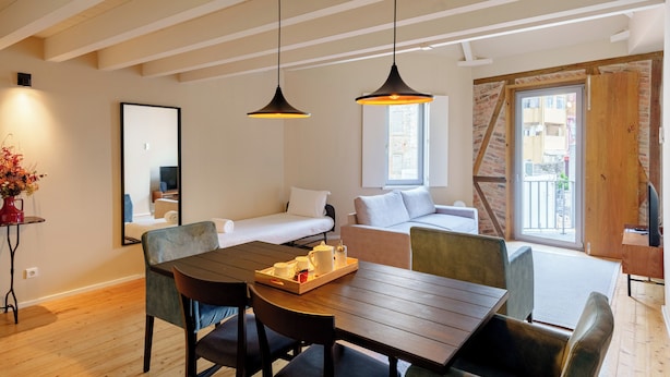 A modern room with a wooden dining table, two pendant lights, a sofa, a bed, and a large window. - Porto Vitoria Apartments (Porto)