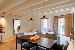A modern room with a wooden dining table, two pendant lights, a sofa, a bed, and a large window.