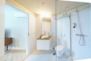 Un bany modern amb una dutxa de vidre, un lavabo blanc amb taulell de fusta i una zona de vàters separada.