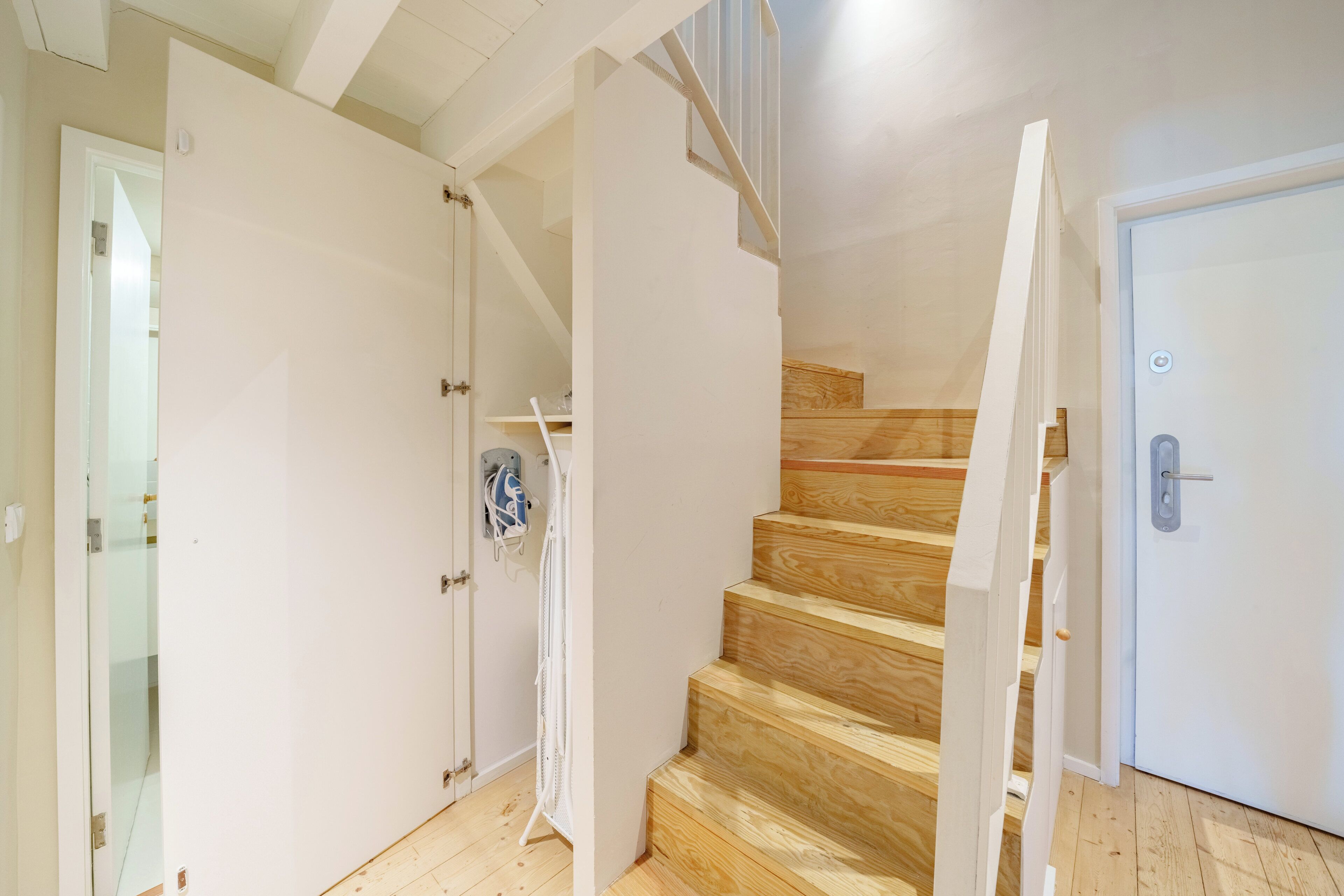 Eine Treppe mit Holzbalken, die zu einer Zwischenebene führt, eine weiße Tür und eine Glastür.
