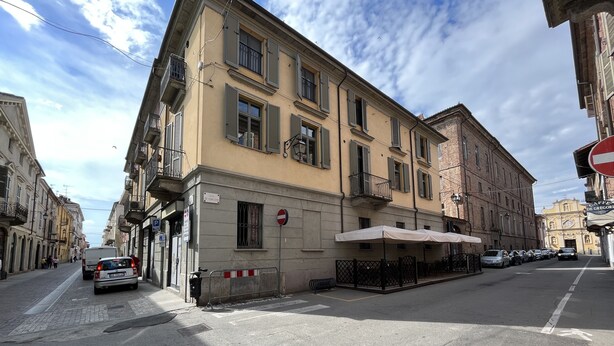 A street view with a building featuring a cafe terrace, a no entry sign, and parked cars.