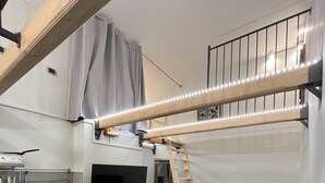 A compact living space with a kitchenette, a sofa, a TV, and a loft area with a ladder.
