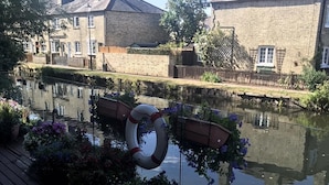 A riverside view with a wooden deck, a floating object, and brick buildings in the background. - Hertford - Sleeps 2 - 92 Walking Score - Garden (Hertford)