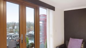 A modern living room with a sliding glass door leading to an outdoor deck, a black leather sofa, and a ceiling light fixture. - Hertford - Sleeps 2 - 92 Walking Score - Garden (Hertford)