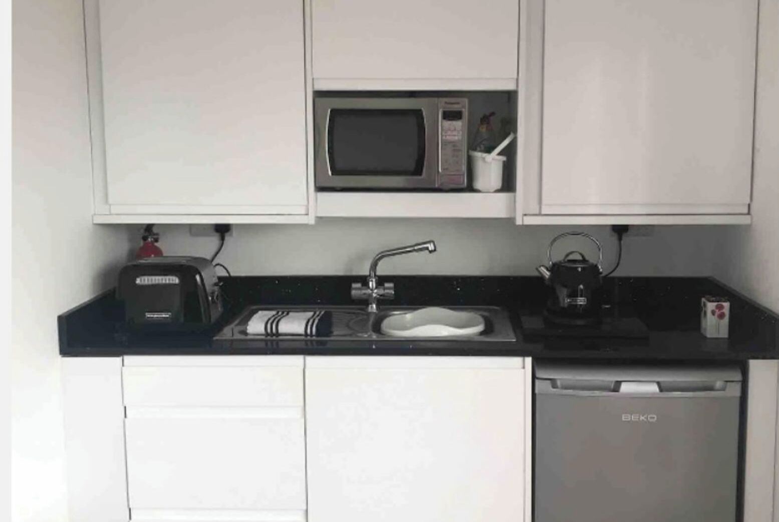 A compact kitchenette with a microwave, toaster, sink, and a small dish rack.