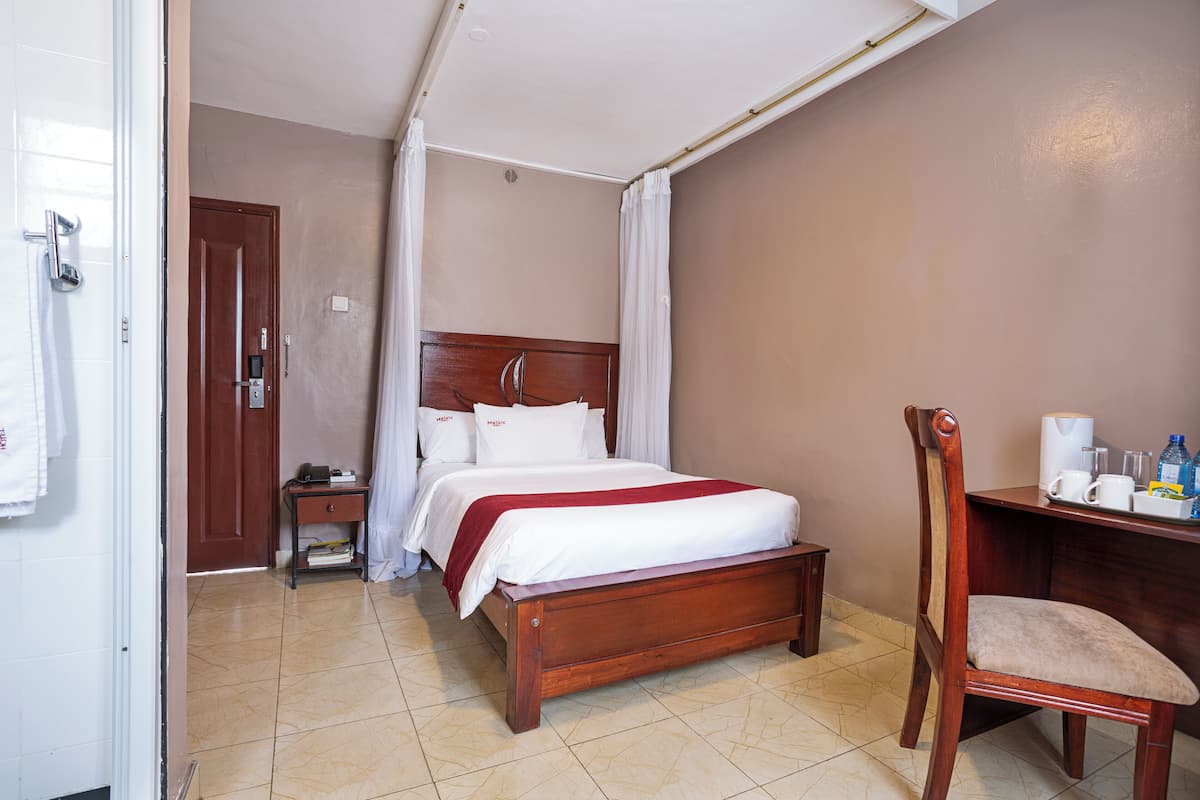 Ein Hotelzimmer mit einem hölzernen Bett, einem Nachttisch, einem Sessel und einem Schreibtisch mit Stuhl.
