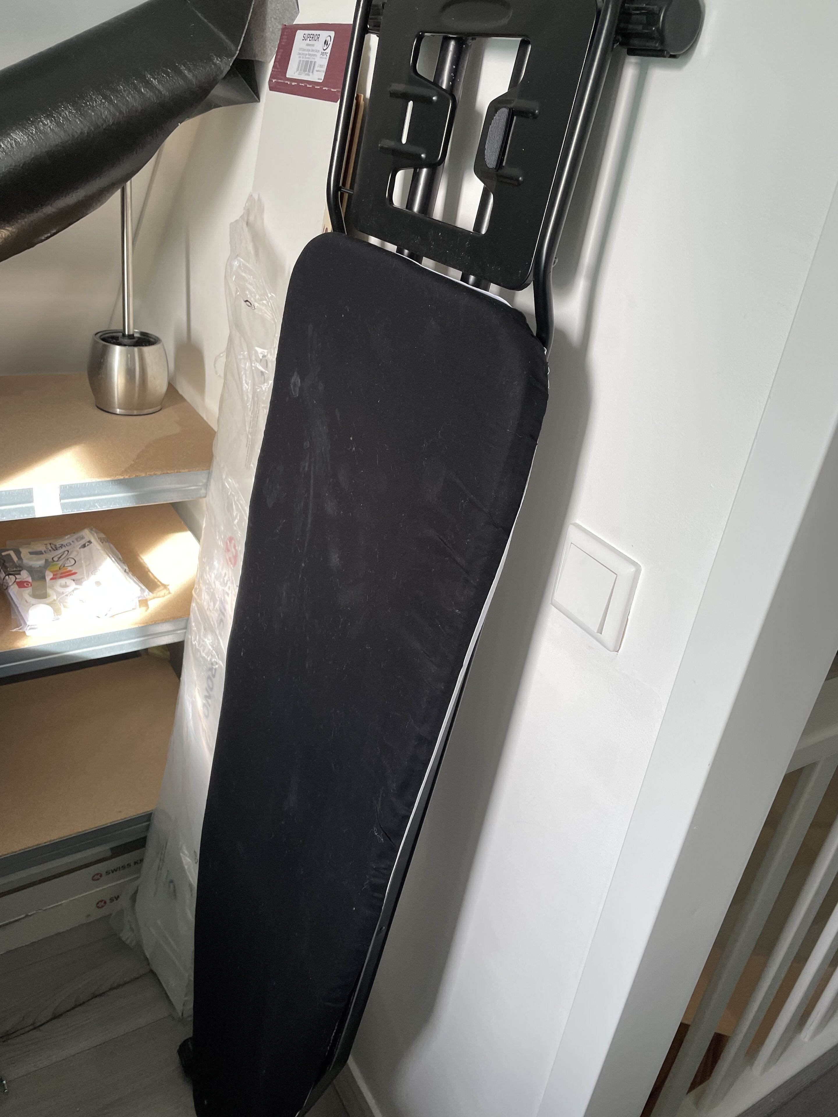 A black ironing board with a metal stand and a white wall in the background.
