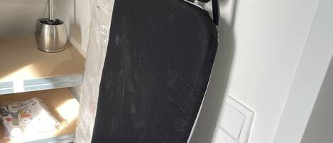 A black ironing board with a metal stand and a white wall in the background.
