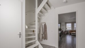 Un interior moderno con una escalera, una sala de estar con sofá y mesa de centro, y un pasillo con perchero.
