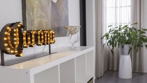 Una sala de estar moderna con una consola blanca, un cuadro abstracto grande, una planta en maceta y un ventanal con cortinas.