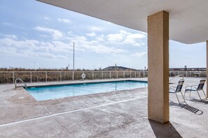 Une piscine avec une plage en béton, des garde-corps en métal et des chaises longues.