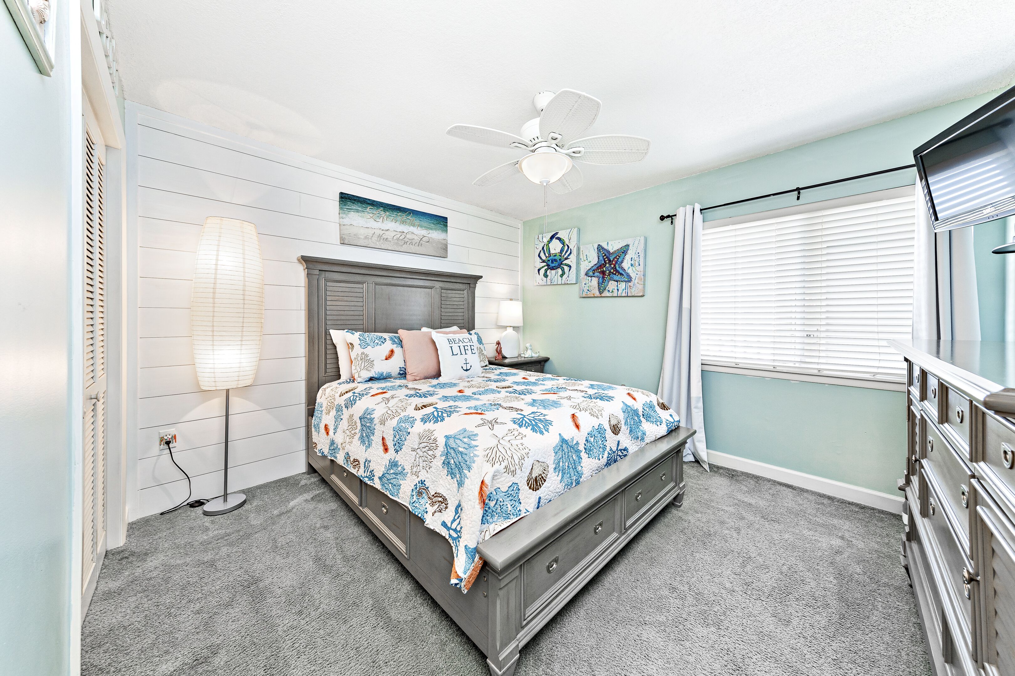 A bedroom with a bed, a nightstand, a dresser, a ceiling fan, and a window with blinds.