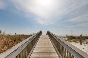 Une promenade en bois qui mène à une plage de sable bordée de dunes.