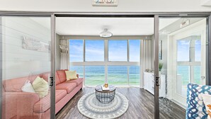 Ein Wohnzimmer mit großem Fenster und Meerblick, ein rosafarbenes Sofa, ein runder Couchtisch und der Blick auf das Meer.