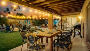 Un patio esterno con tavolo e sedie in legno, luci a tendina e un murale sulla parete.