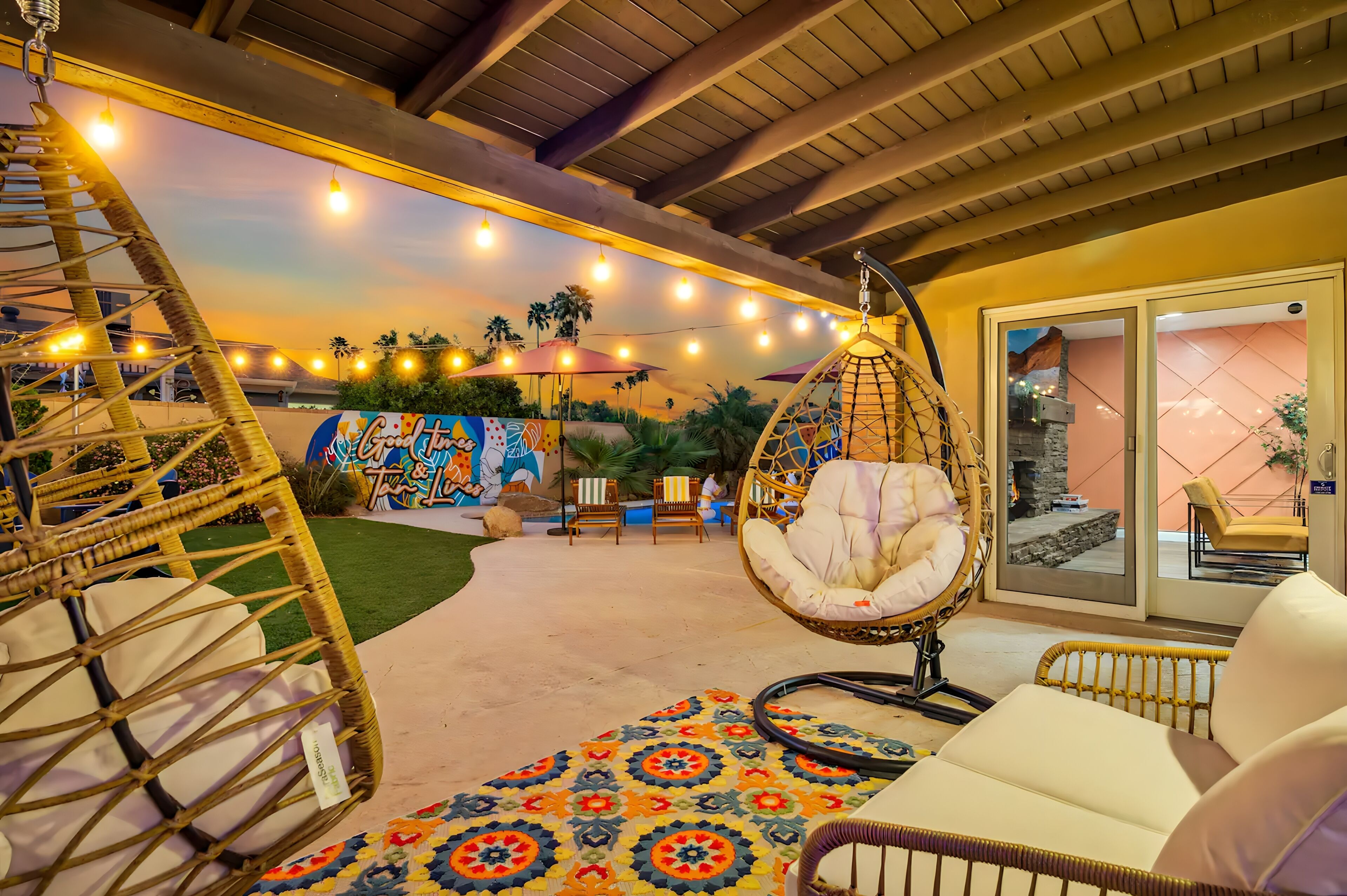 A cozy outdoor seating area with wicker chairs and a hanging chair, a colorful rug, and string lights.