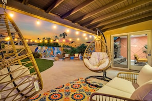A cozy outdoor seating area with wicker chairs and a hanging chair, a colorful rug, and string lights.