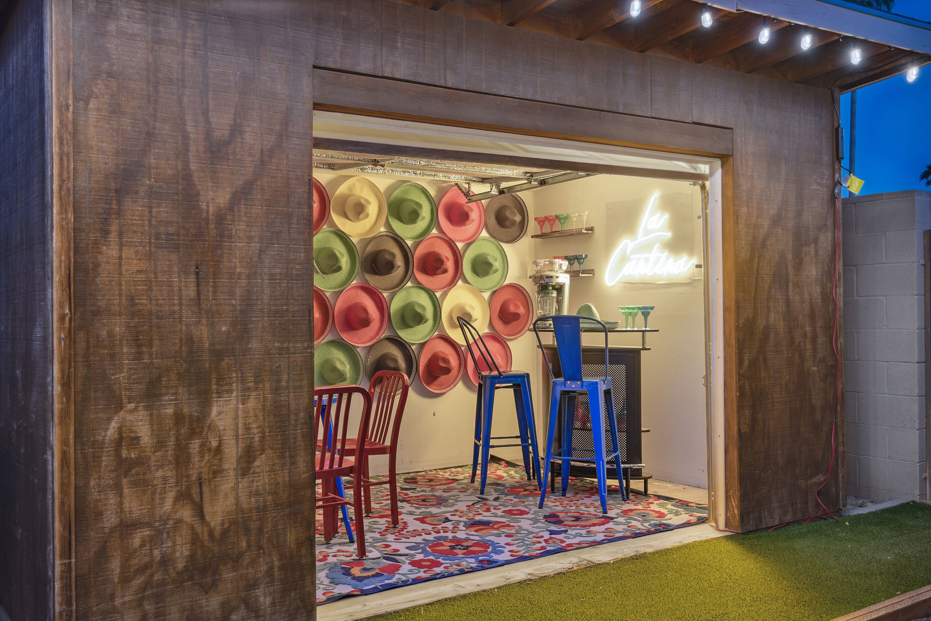 A room with a wooden wall, a neon sign, and a wall of colorful hats.