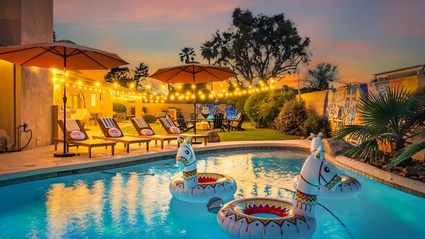 Una piscina con gonfiabili a forma di unicorno, sedie a sdraio e luci decorative.