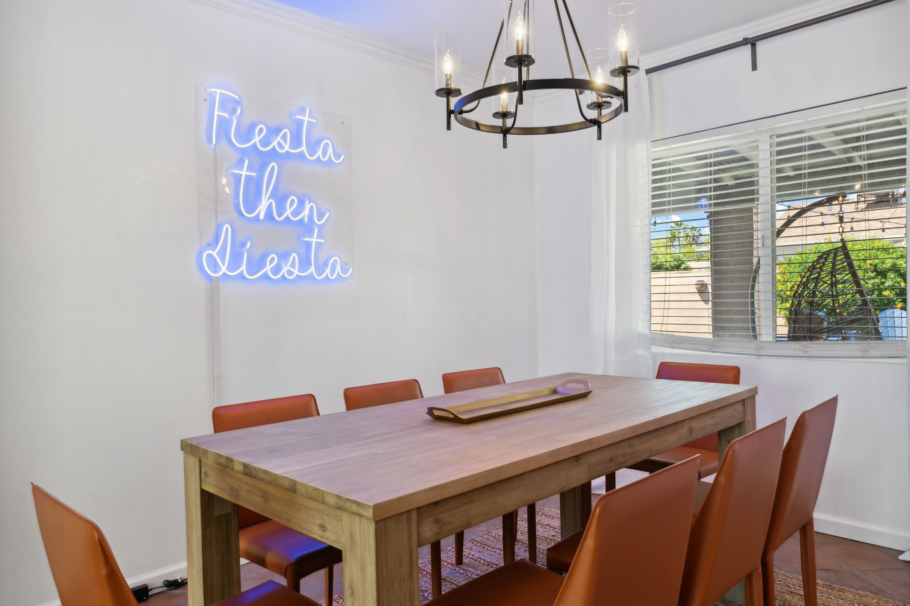 Un espace repas avec une table en bois, des chaises orange, un néon et un lustre.