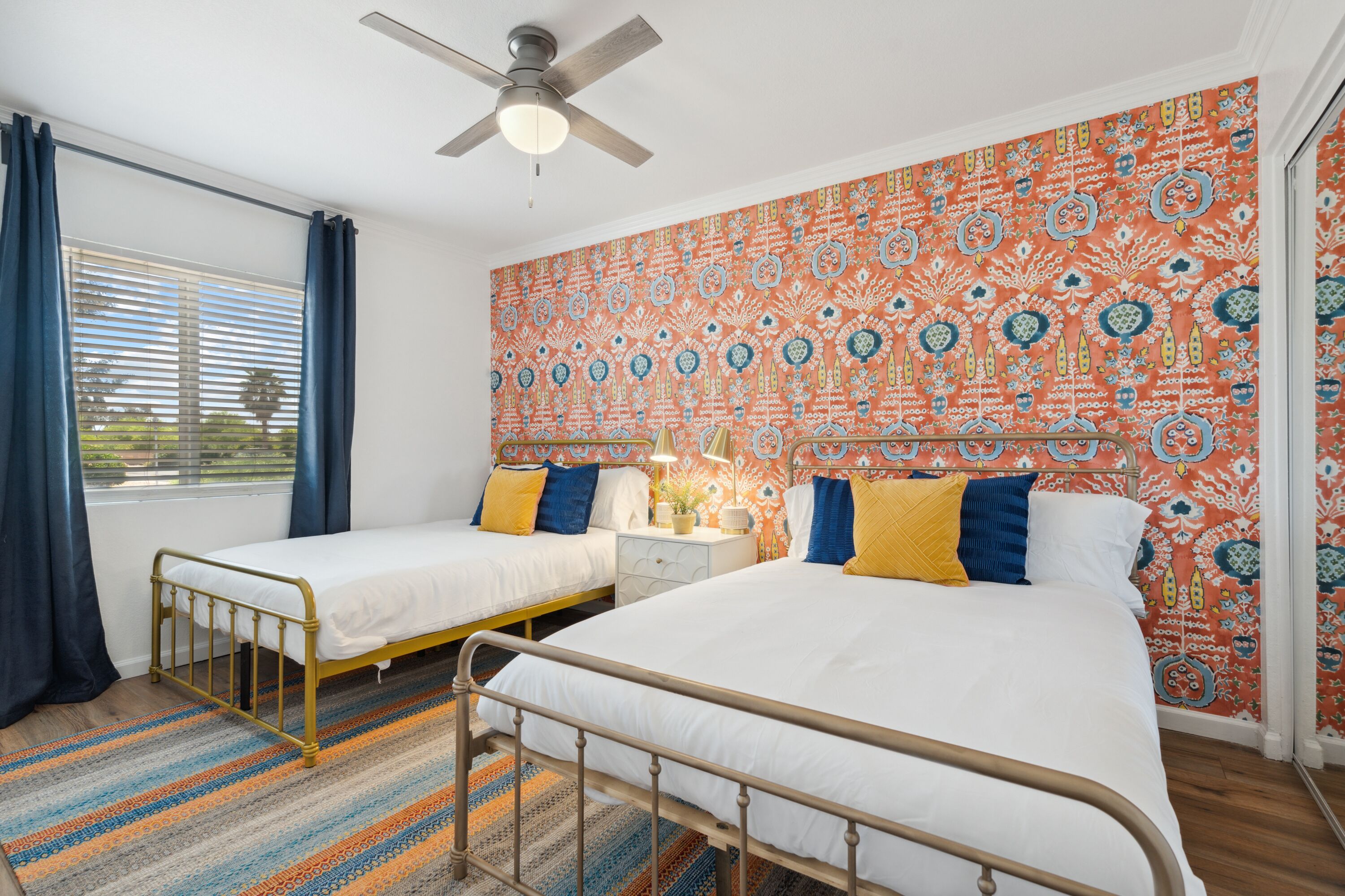 A bedroom with two beds, a ceiling fan, and patterned wallpaper.