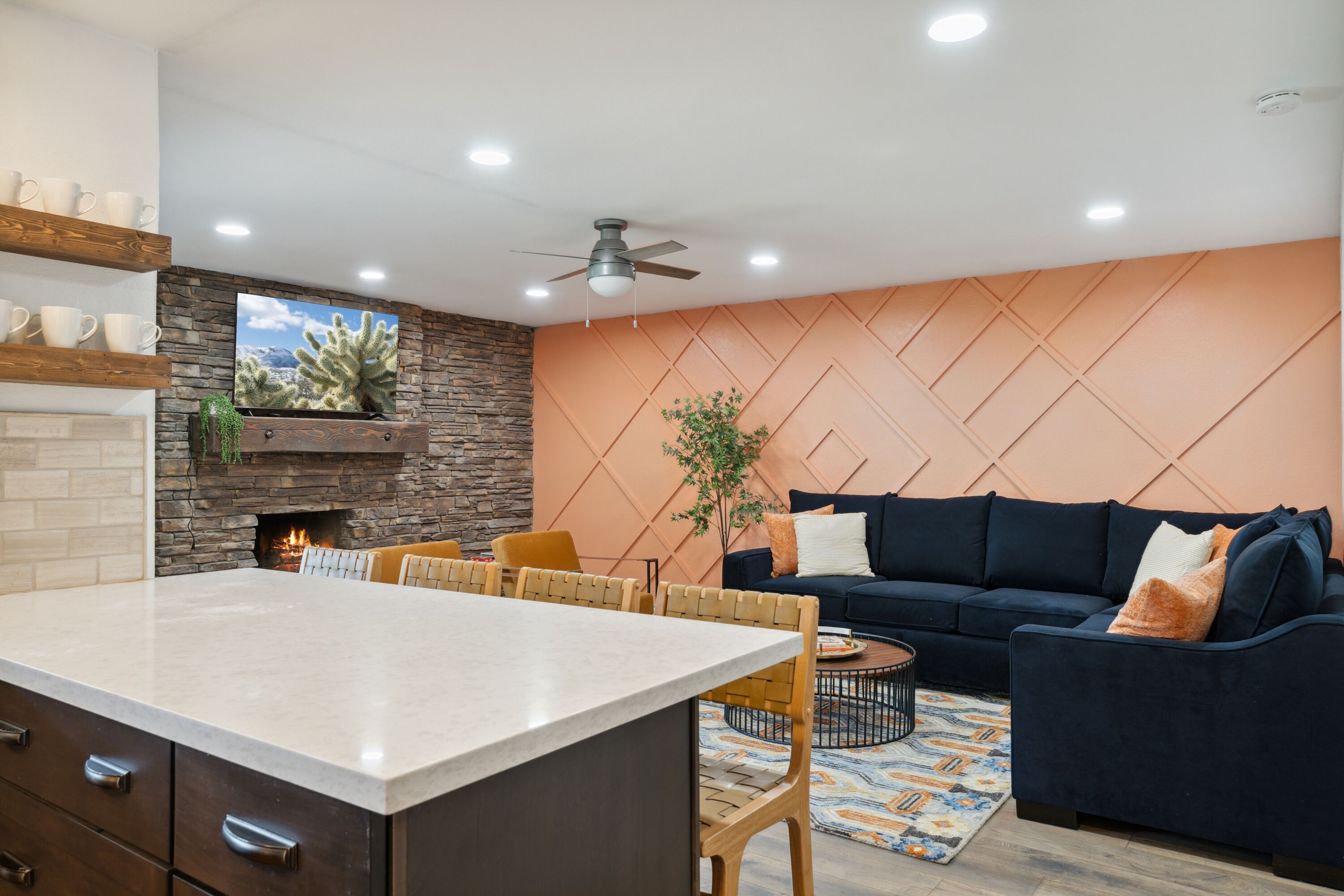 Una cocina moderna con una isla central, un comedor con sillas de madera, un sofá azul oscuro y una chimenea.