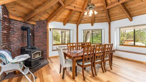 Un comedor con una mesa y sillas de madera, una chimenea de ladrillo y ventanas amplias.