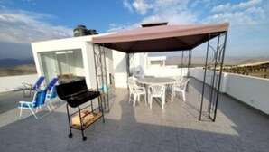 Una terraza en la azotea con zona de barbacoa, mobiliario exterior y vistas al paisaje.