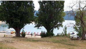 Une plage au bord d’un lac, avec des arbres, une jetée et des chaises de plage.