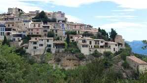 Un village perché sur une colline, avec des bâtiments en pierre, dont certains sont dotés de balcons, et un paysage montagneux en arrière-plan.