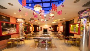 A spacious restaurant with multiple tables and chairs, a central chandelier, and decorative elements on the ceiling. - Aristro Club (Alipur)