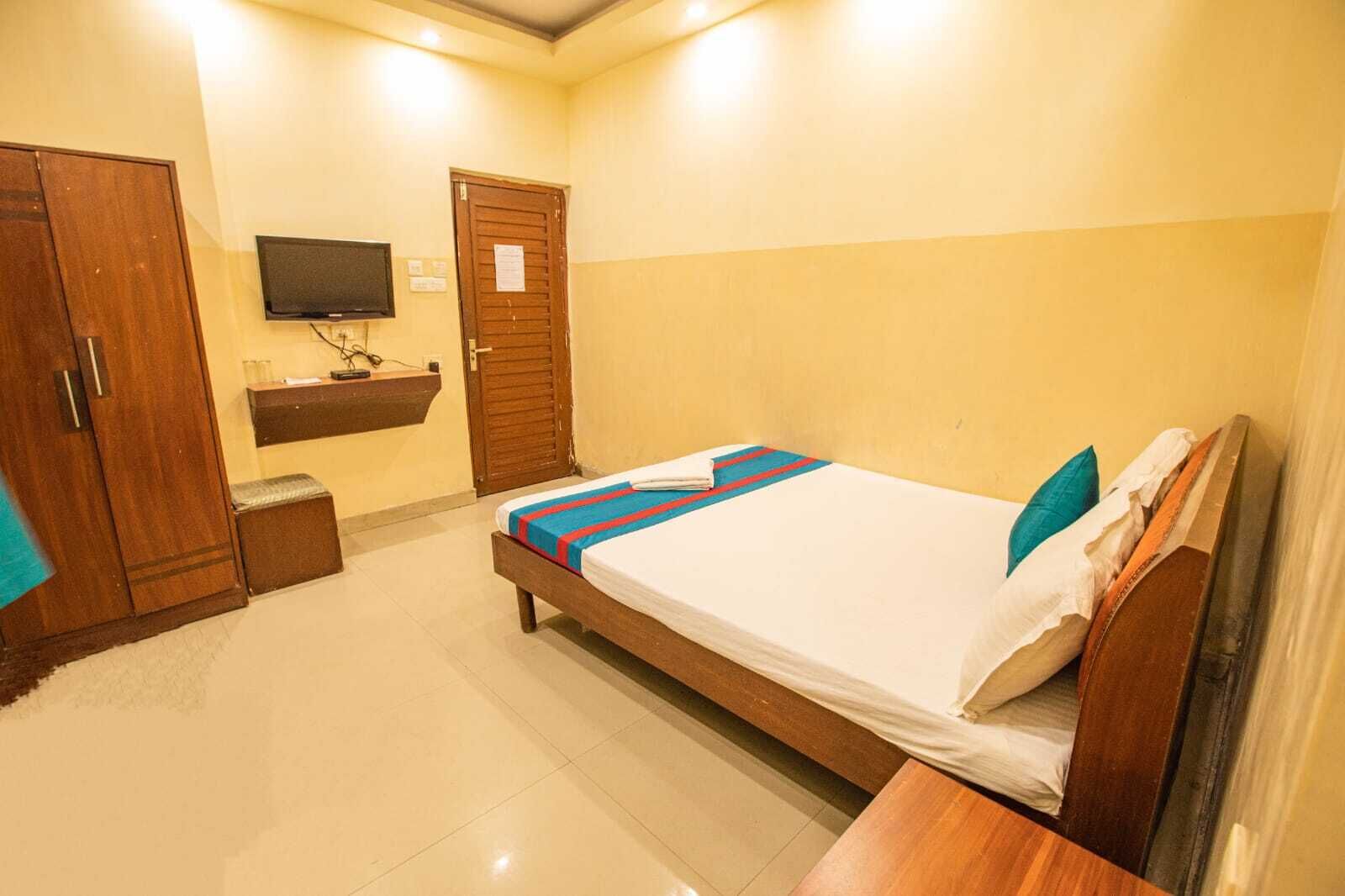 A bedroom with a bed, wooden wardrobe, a television, and a small desk.