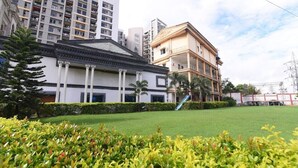 A building with a classical facade, a green lawn, and a modern high-rise in the background. - Aristro Club (Alipur)
