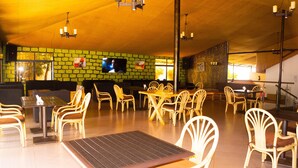 A spacious indoor area with multiple seating arrangements, including tables and chairs, and a large screen mounted on the wall. - Distinction Gardens (Siaya)