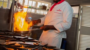 A chef cooking with a large flame on a stove in a kitchen. - Distinction Gardens (Siaya)