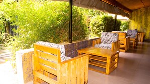 A covered outdoor seating area with wooden furniture and a backdrop of dense green foliage. - Distinction Gardens (Siaya)