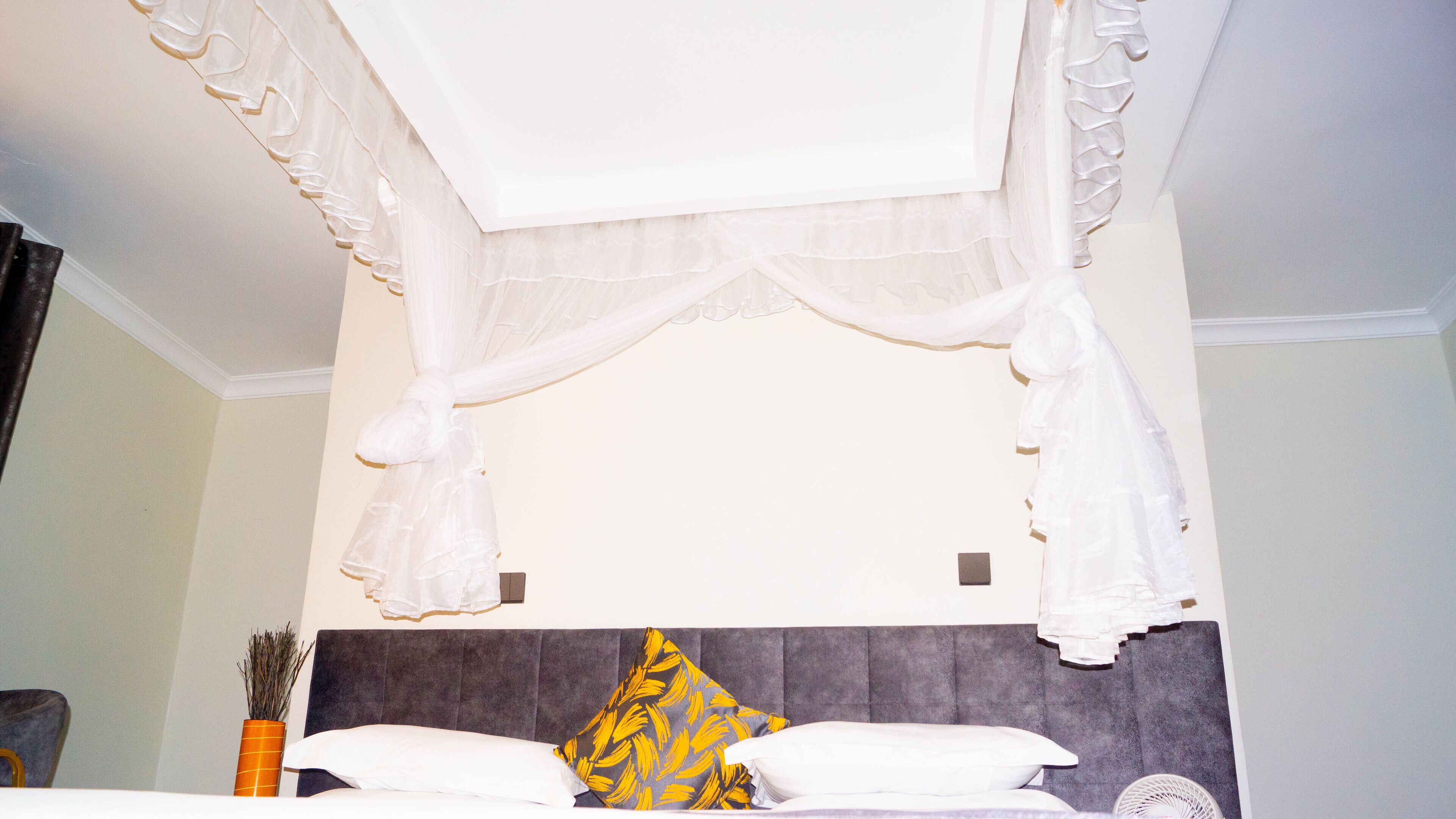 A bed with white bedding, a grey headboard, and a decorative yellow pillow.