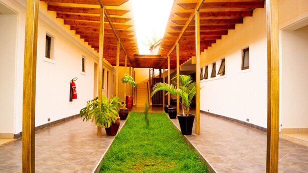 A corridor with a central grassy area, wooden beams on the ceiling, potted plants, and a fire extinguisher on the wall. - Distinction Gardens (Siaya)