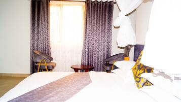Une chambre d’hôtel avec un lit, deux fauteuils, une petite table ronde et un rideau.