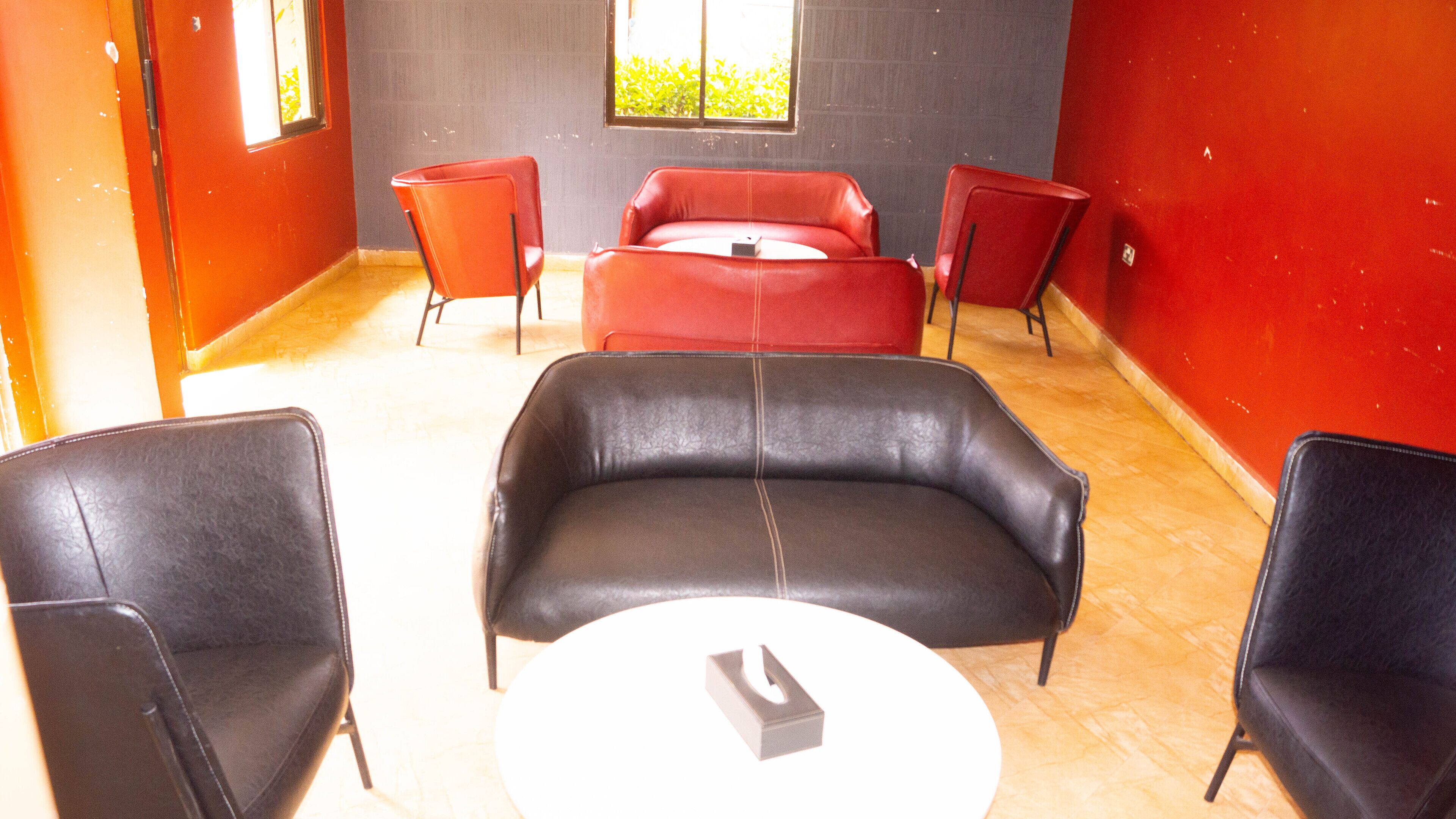 Una habitación con un sofá de cuero negro, dos sillas rojas y una mesa blanca.
