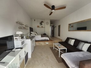 Un espacio habitable compacto con kitchenette, cama, sofá y ventilador de techo.