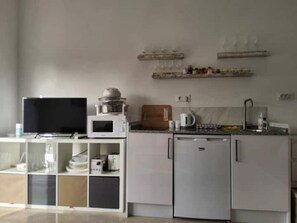 Una cocina compacta con microondas, un refrigerador pequeño, un lavamanos y un televisor.