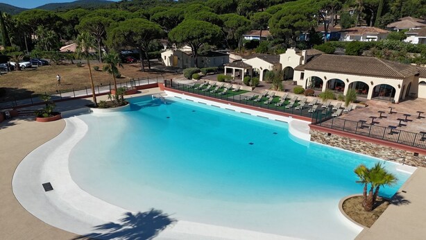 A large, curved swimming pool with a white edge, surrounded by lounge chairs and a covered patio area.