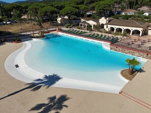 Une grande piscine incurvée, bordée de blanc, entourée de chaises longues et d’un espace patio couvert.