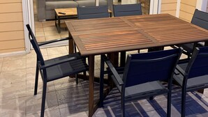 An outdoor dining area with a wooden table and chairs, a sofa, and a television in the background.