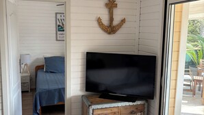 A room with a bed, a television on a wooden chest, a wall-mounted anchor decoration, and a door leading to another room.